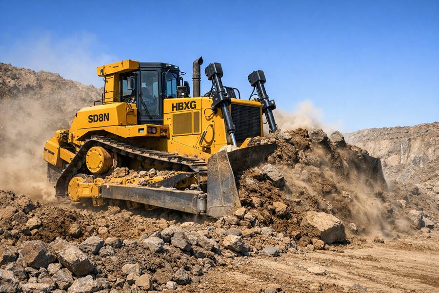 A yellow HBXG SD8N bulldozer with an elevated sprocket design actively pushing large piles of earth and rocks in a dusty mining quarry under a clear blue sky.